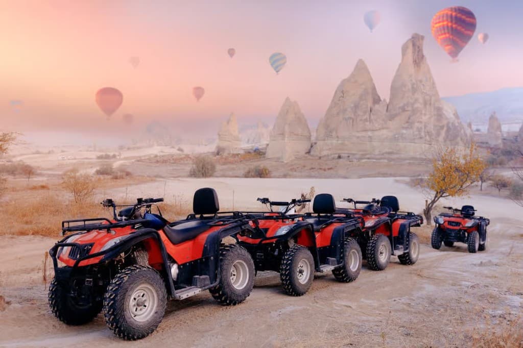 Quad bikes parked among fairy chimneys with hot air balloons at dawn on the bookable Göreme Quad Safari from The Owl Cave Hotel, Cappadocia