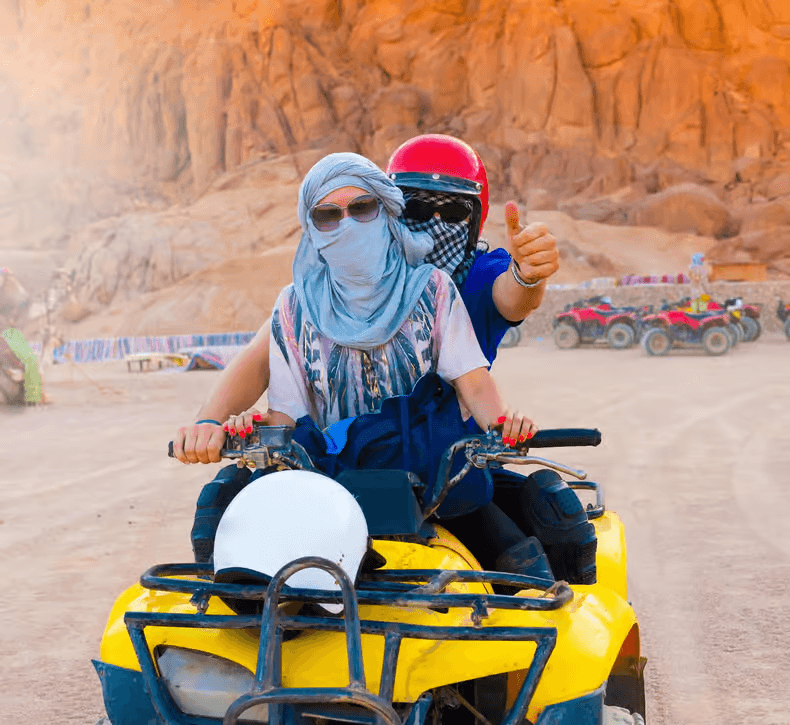 Two guests sharing an ATV with helmets and a dust scarf on the bookable Göreme Quad Safari from The Owl Cave Hotel