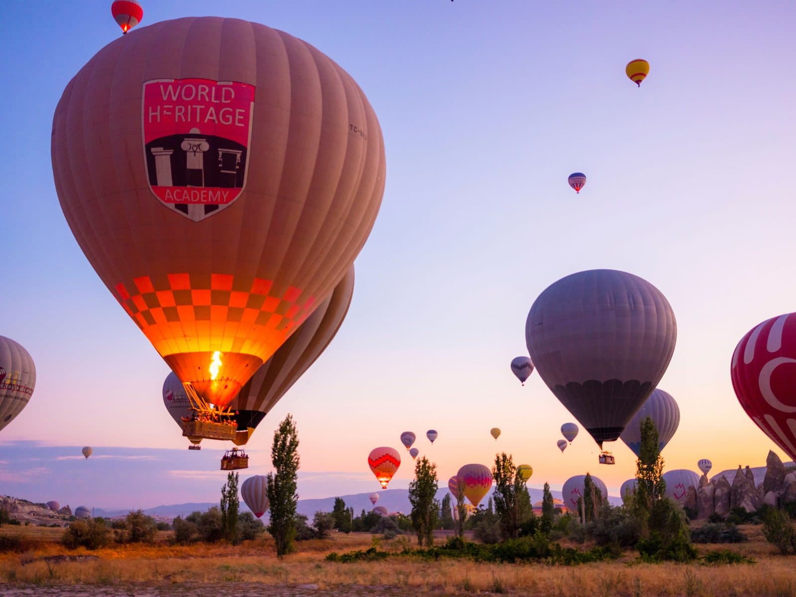A balloon envelope with the burner lit, other balloons at sunrise. Sunrise Horse Ride, arranged from The Owl Cave Hotel in Göreme, Cappadocia.