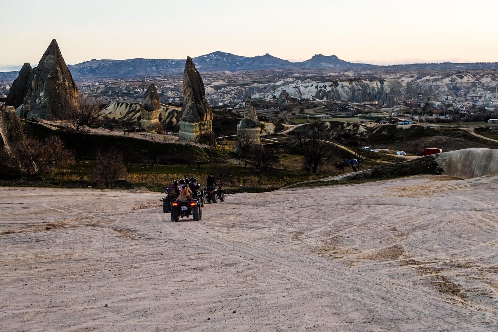 ATVs riding across a dusty plain toward fairy chimneys. Sunset ATV Safari, arranged from The Owl Cave Hotel in Göreme, Cappadocia.