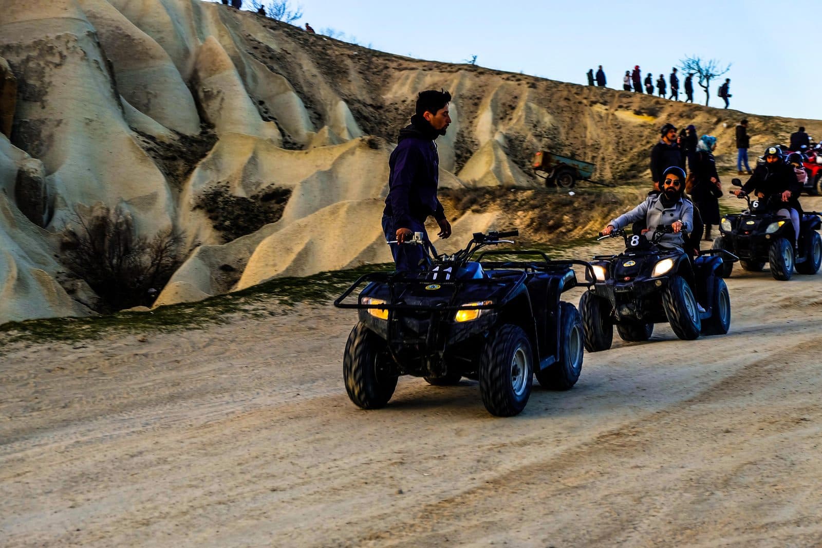 An ATV leading riders along a dirt track through striped hills. Sunset ATV Safari, arranged from The Owl Cave Hotel in Göreme, Cappadocia.
