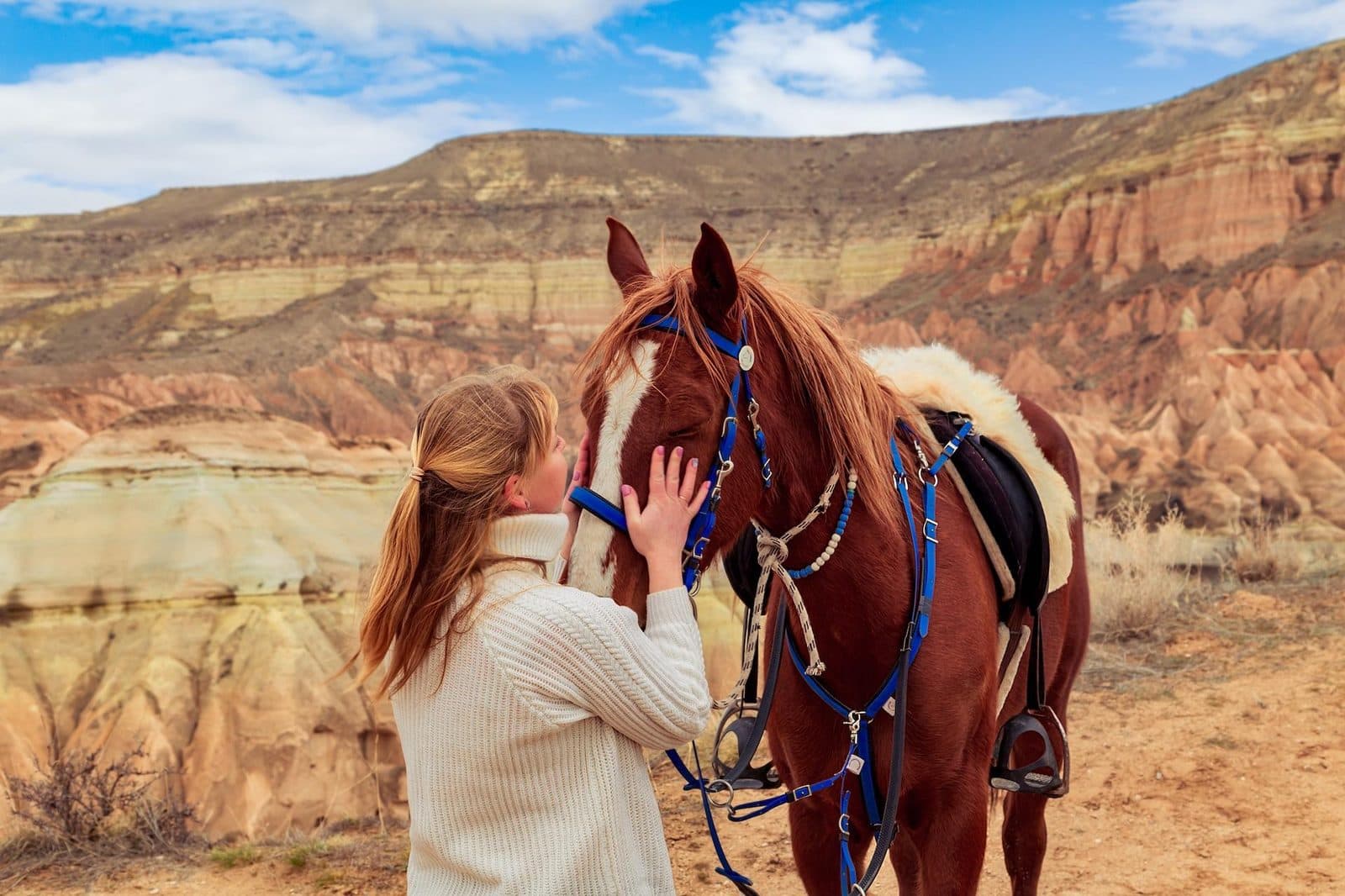 A guest holding a brown horse’s bridle against red hills. Sunset Horse Trek, arranged from The Owl Cave Hotel in Göreme, Cappadocia.