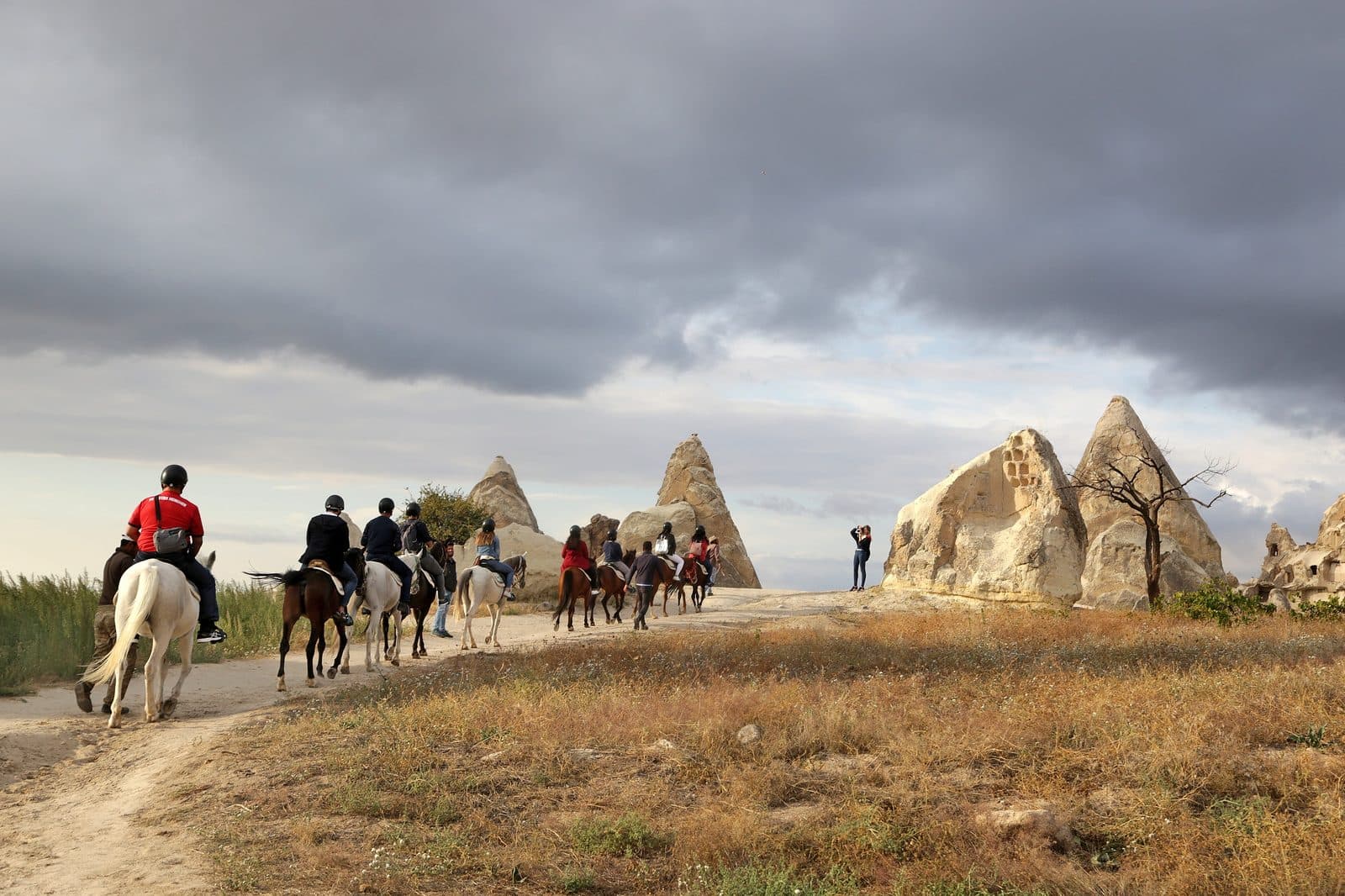Riders on a dirt track under cloud, pale chimneys beside them. Sunset Horse Trek, arranged from The Owl Cave Hotel in Göreme, Cappadocia.