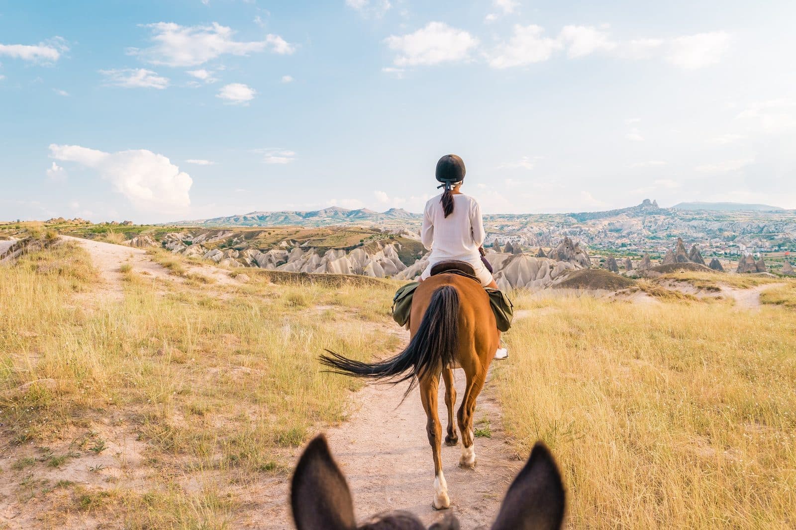 The view from horseback of a rider ahead and a town in the valley. Sunset Horse Trek, arranged from The Owl Cave Hotel in Göreme, Cappadocia.