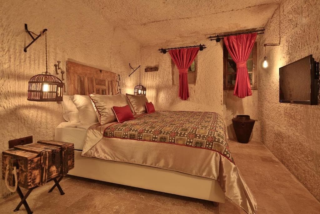 Bookable Cave Suite king bed in a volcanic tuff cave with red curtains at The Owl Cave Hotel, Göreme, Cappadocia
