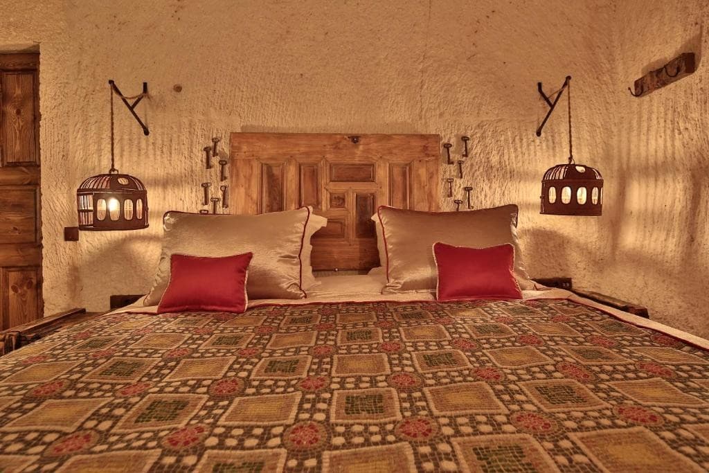 Cave Suite king bed with carved wooden headboard and lantern lighting at The Owl Cave Hotel in Göreme