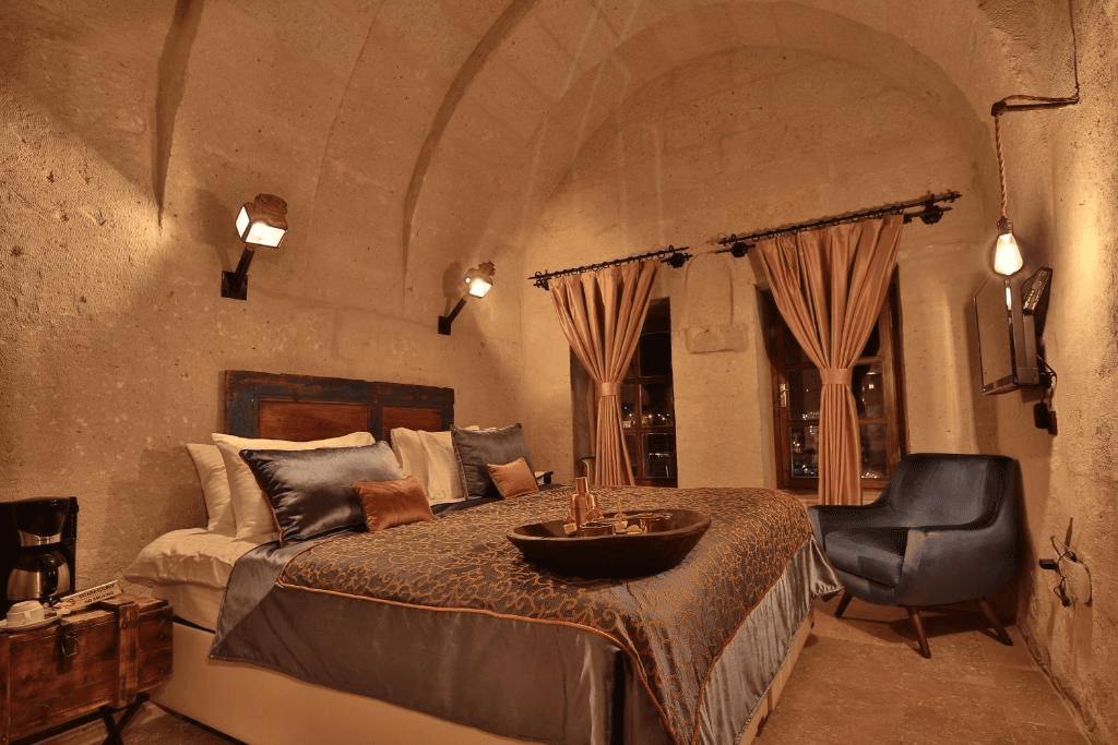 Deluxe Arch Room with View king bed, welcome tray, and gold-curtained windows at The Owl Cave Hotel, Göreme