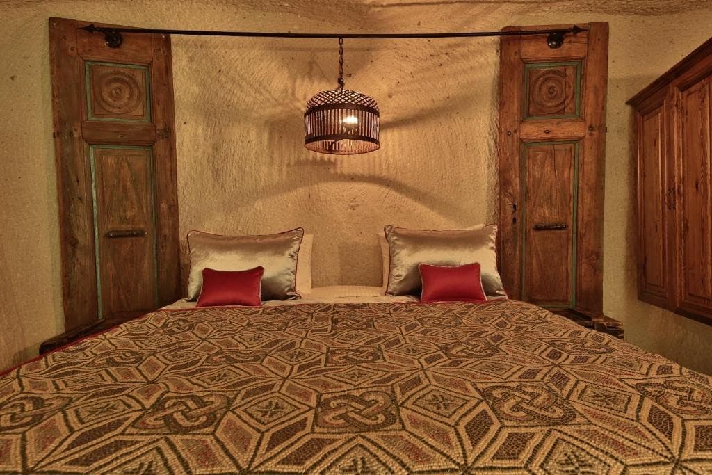 Deluxe King Suite king bed with carved wooden doors at The Owl Cave Hotel in Göreme, Cappadocia