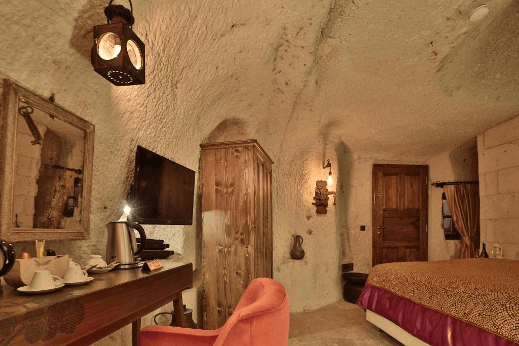 Premier Cave Room cave interior with lantern lighting, desk, and king bed at The Owl Cave Hotel in Göreme