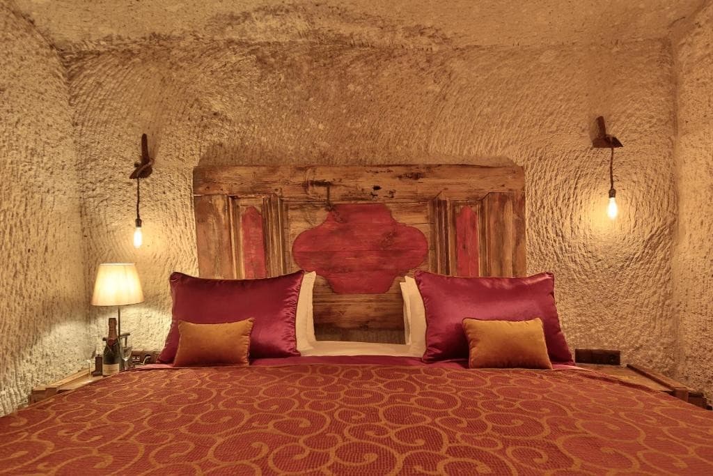 Bookable Superior Cave Room king bed with carved wooden headboard in a volcanic tuff cave at The Owl Cave Hotel, Göreme, Cappadocia
