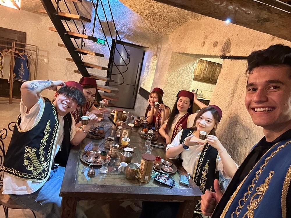 Guests and hosts sharing Turkish coffee at a cave table in The Owl Cave Hotel, Göreme, Cappadocia