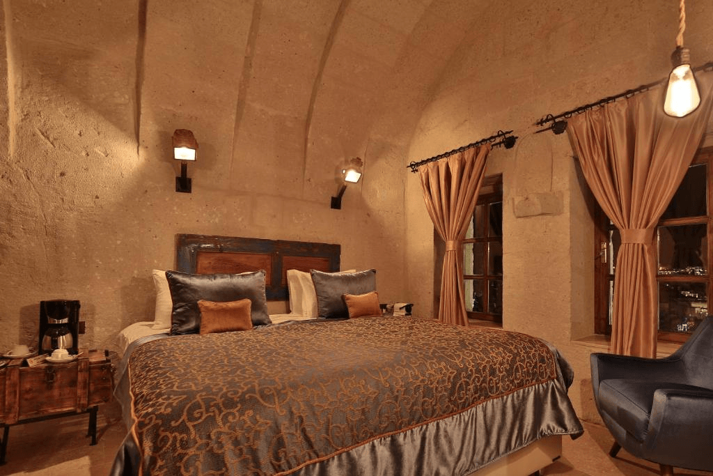 Bookable Deluxe Arch Room with View king bed under a tuff arch, with balcony windows, at The Owl Cave Hotel in Göreme, Cappadocia
