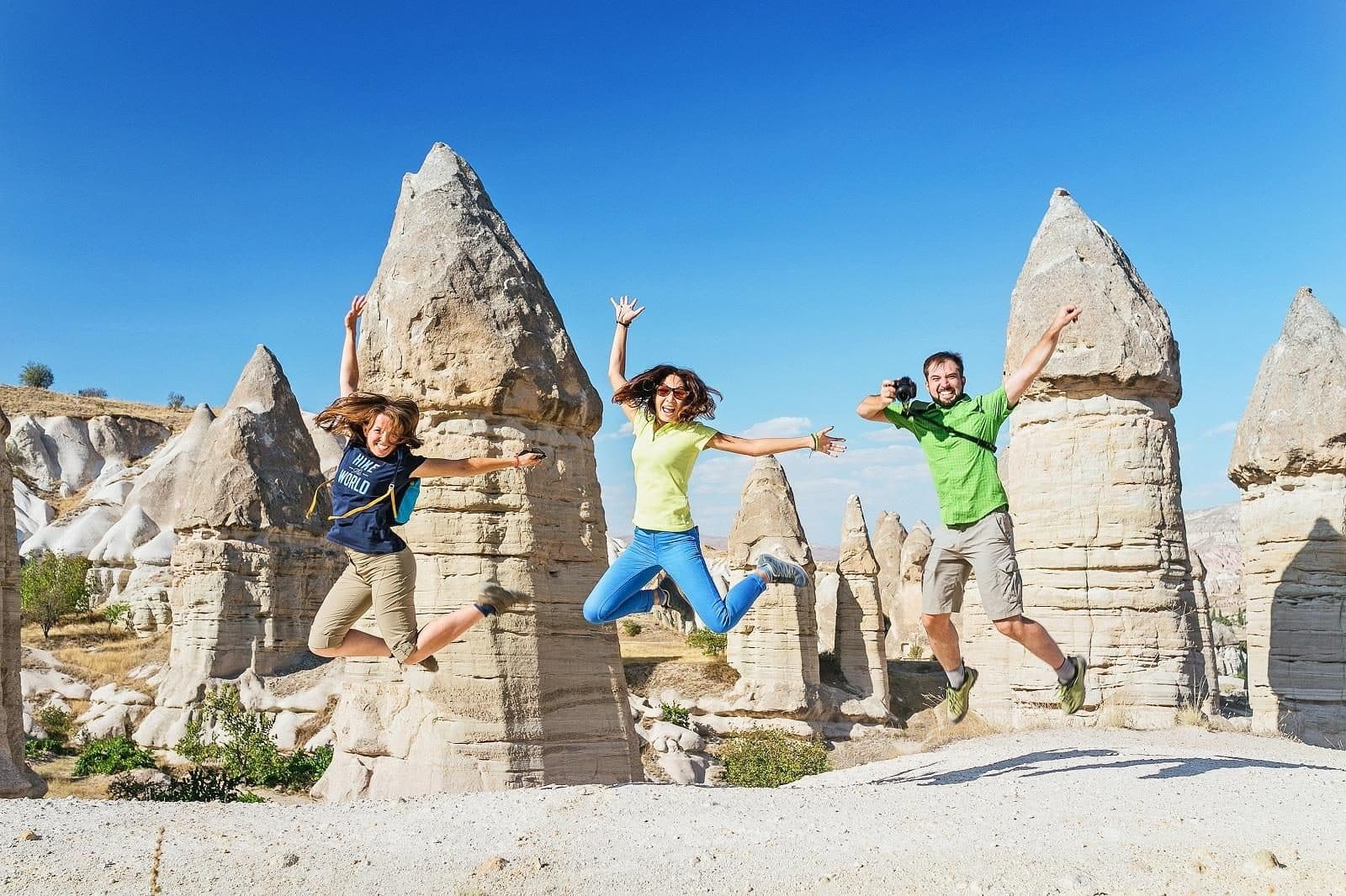 Three guests jumping in front of fairy chimneys. Sunrise Balloon and Cappadocia Day, arranged from The Owl Cave Hotel in Göreme, Cappadocia.