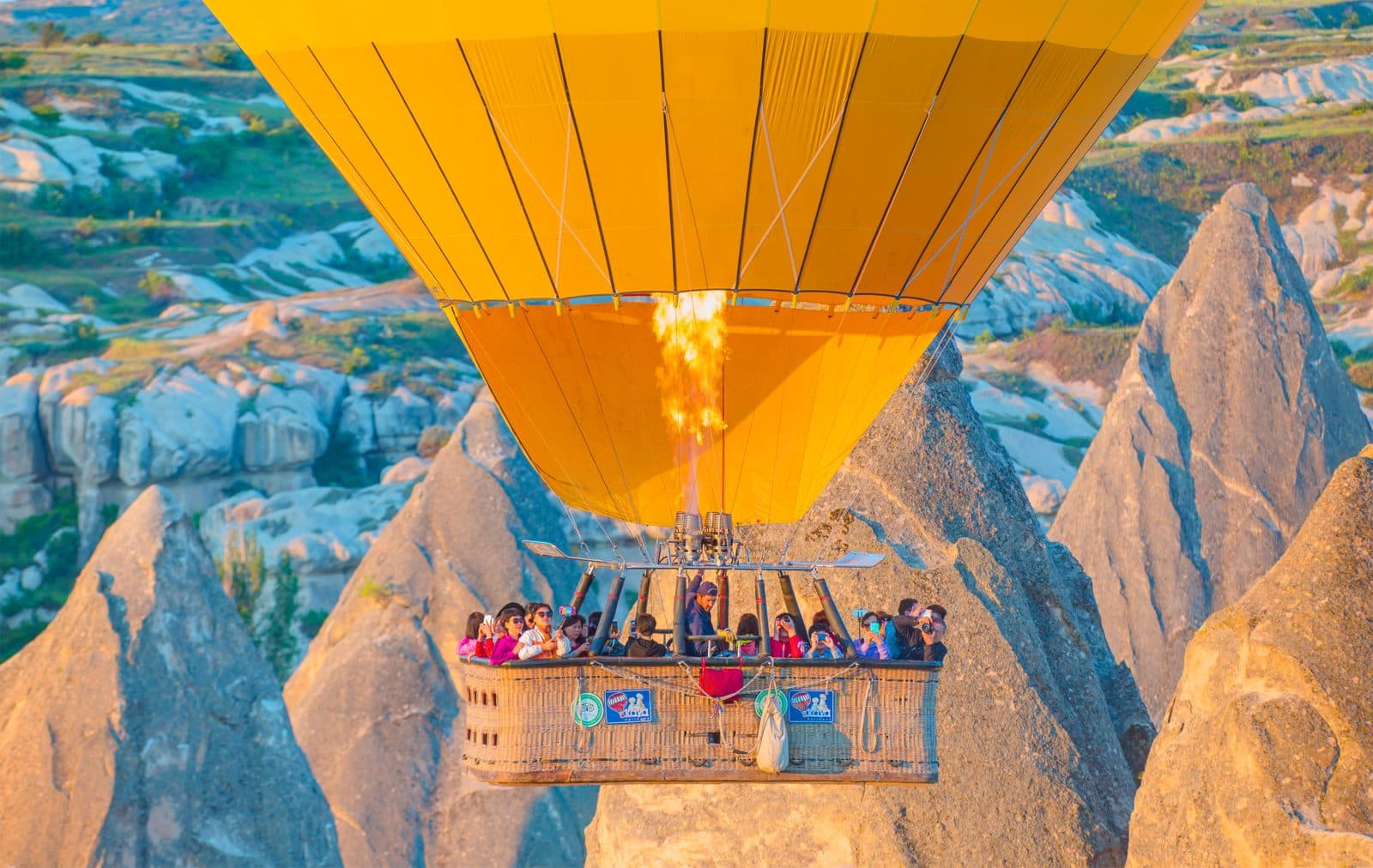 A yellow hot air balloon basket flying over fairy chimneys. Sunrise Balloon and Cappadocia Day, arranged from The Owl Cave Hotel in Göreme, Cappadocia.