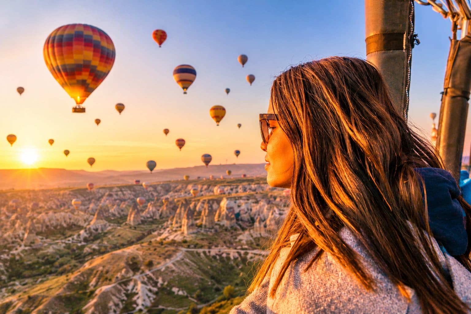 A guest in profile with hot air balloons at sunrise over the valleys. Balloon Flight with a Choice of Day Tour, arranged from The Owl Cave Hotel in Göreme, Cappadocia.