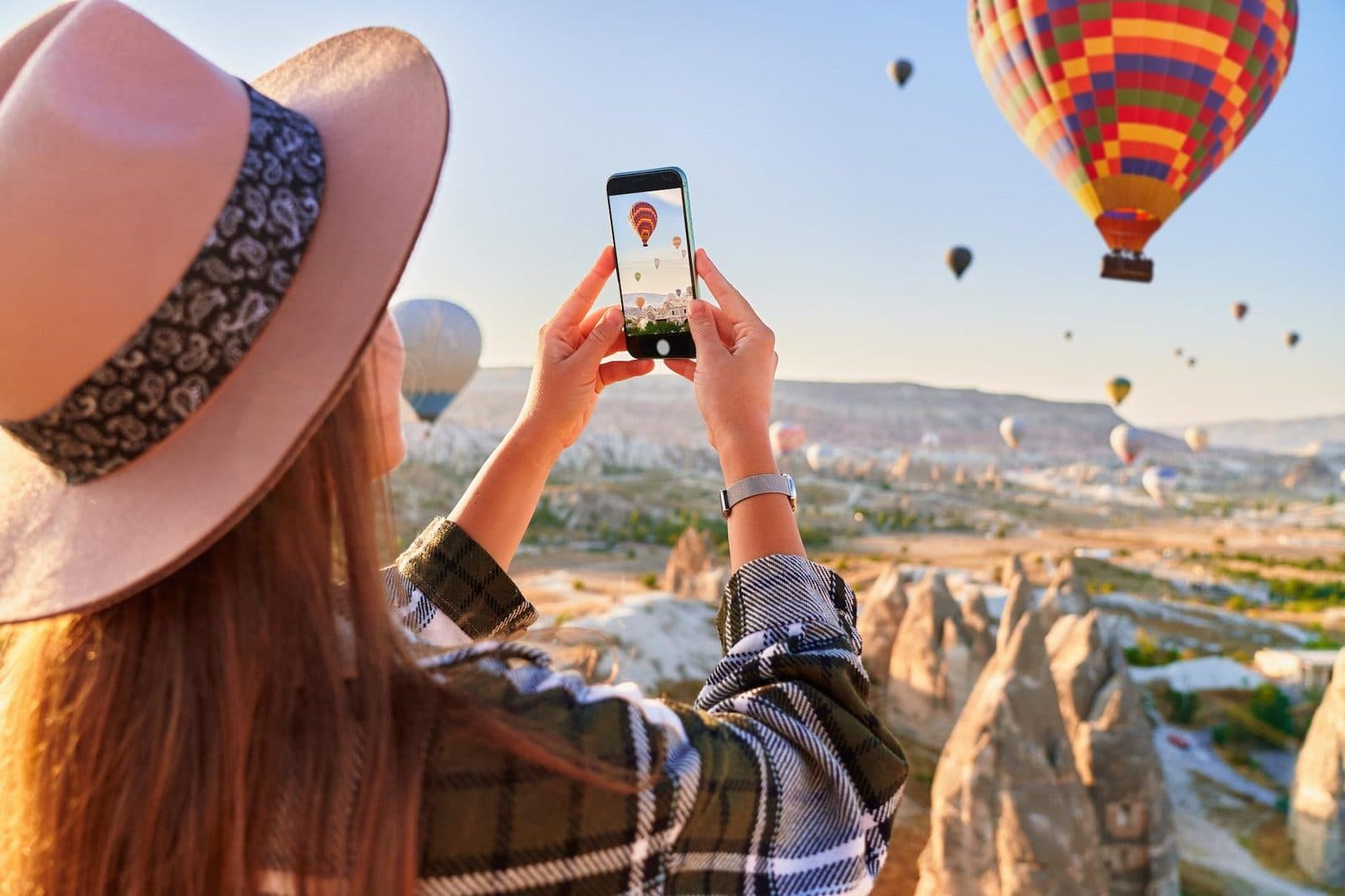 A guest in a hat photographing a hot air balloon. Cappadocia from Antalya, arranged from The Owl Cave Hotel in Göreme, Cappadocia.