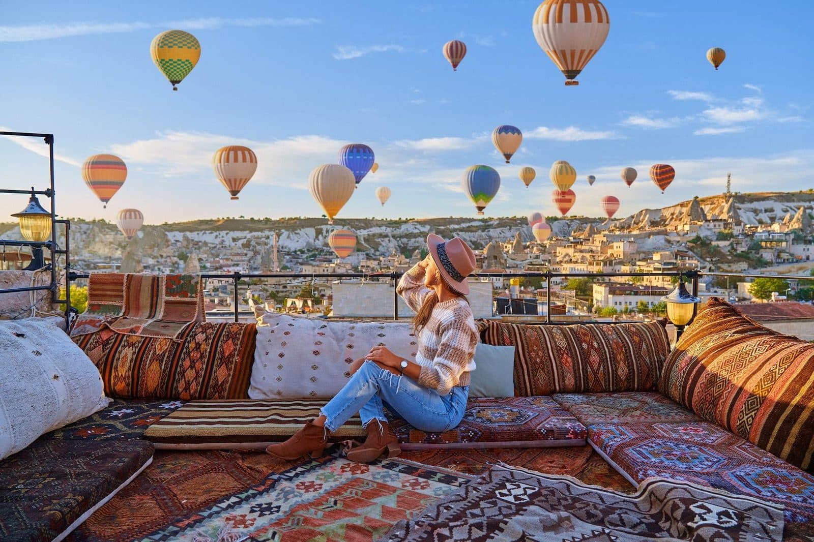 A guest on a terrace sofa with balloons above the town. Cappadocia from Antalya, arranged from The Owl Cave Hotel in Göreme, Cappadocia.