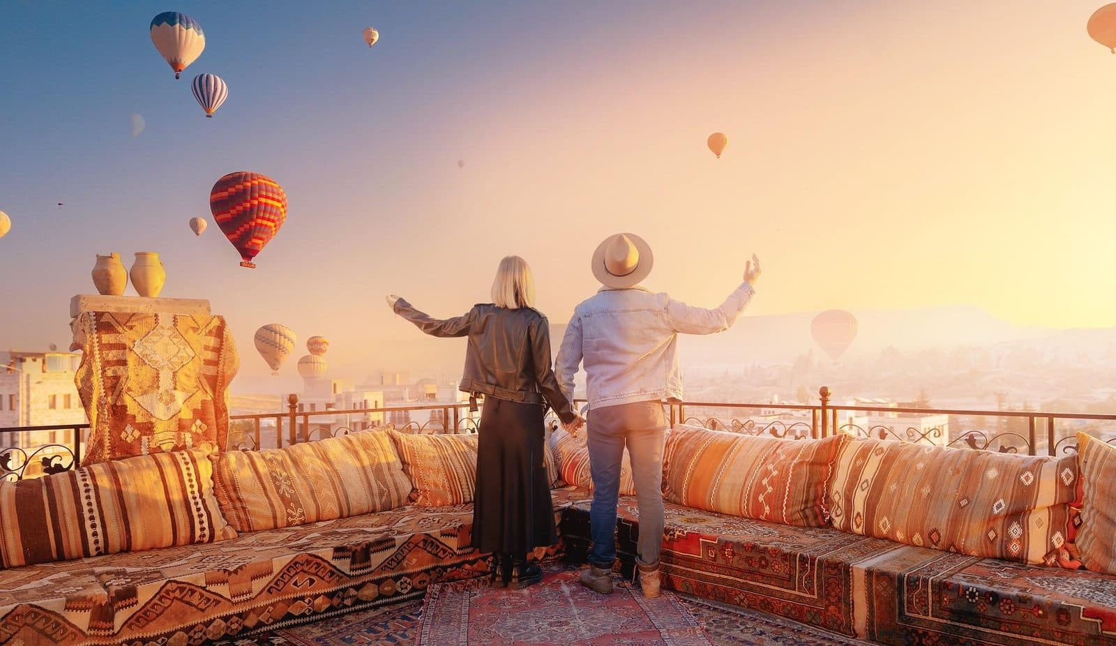A couple on a terrace at sunrise, balloons over the town. Cappadocia from Antalya, arranged from The Owl Cave Hotel in Göreme, Cappadocia.