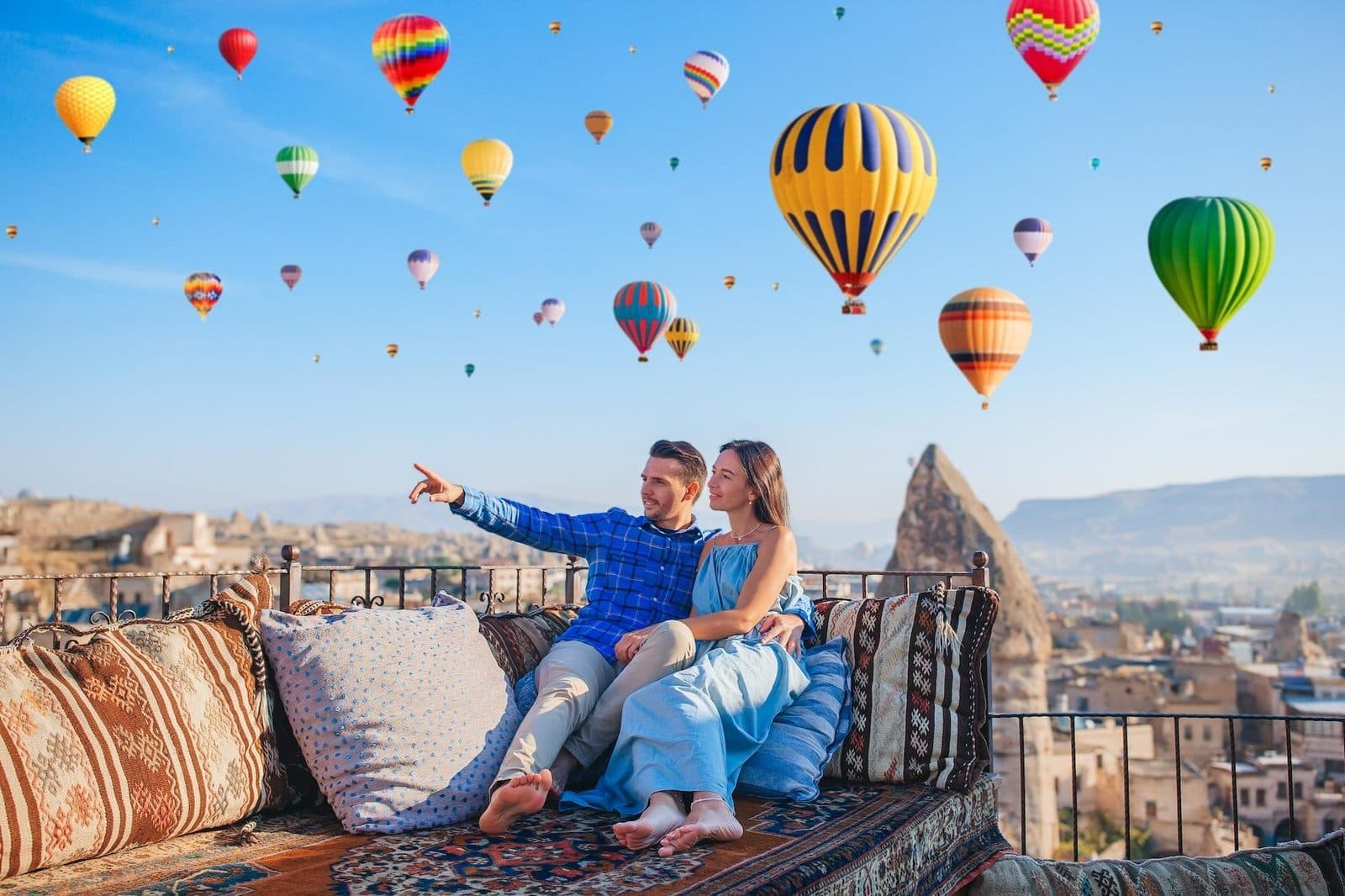 A couple on a terrace sofa pointing at hot air balloons. Cappadocia from Istanbul, arranged from The Owl Cave Hotel in Göreme, Cappadocia.