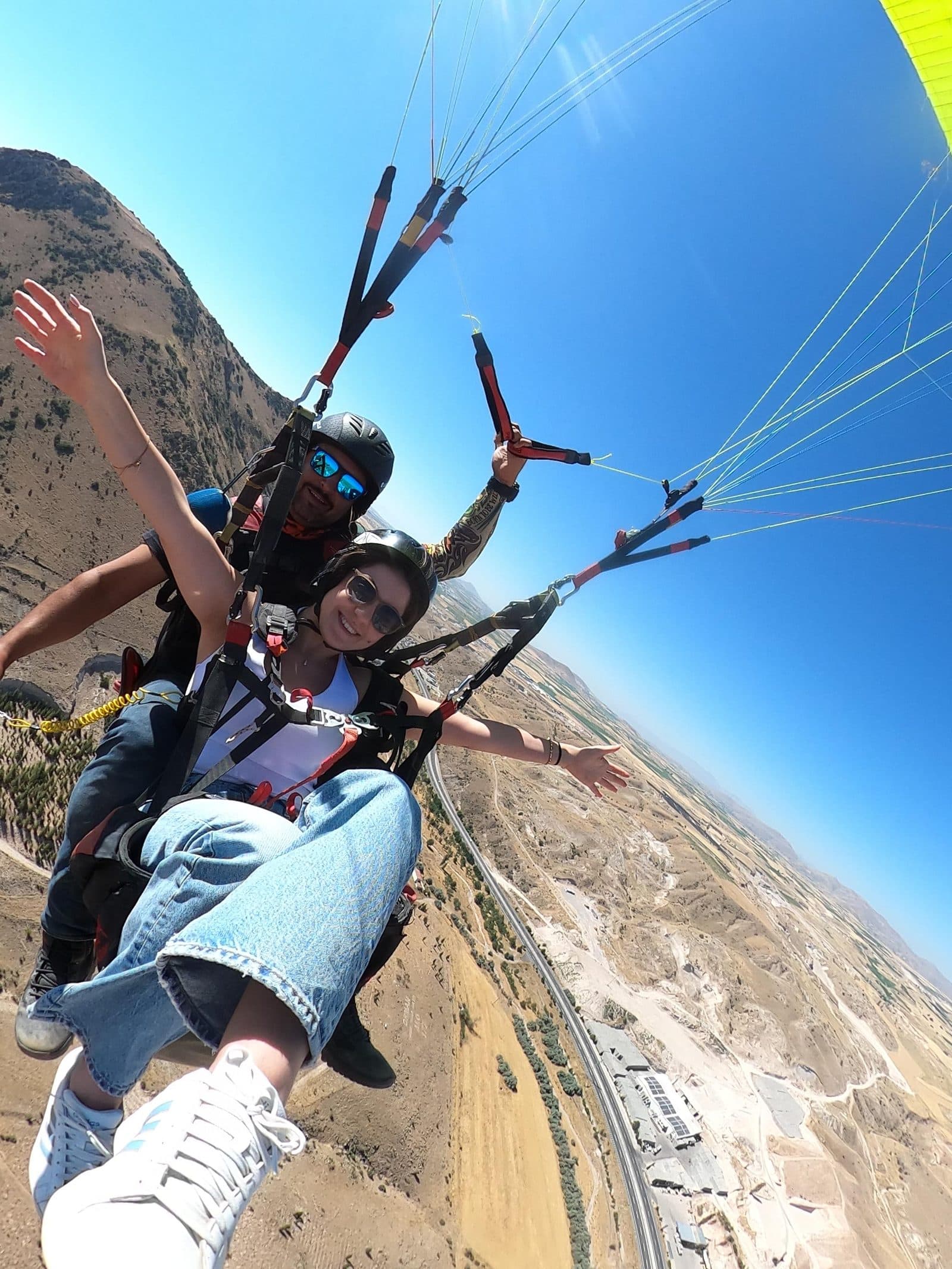 A passenger’s jeans and white sneakers, with fields far below. Tandem Paragliding, arranged from The Owl Cave Hotel in Göreme, Cappadocia.