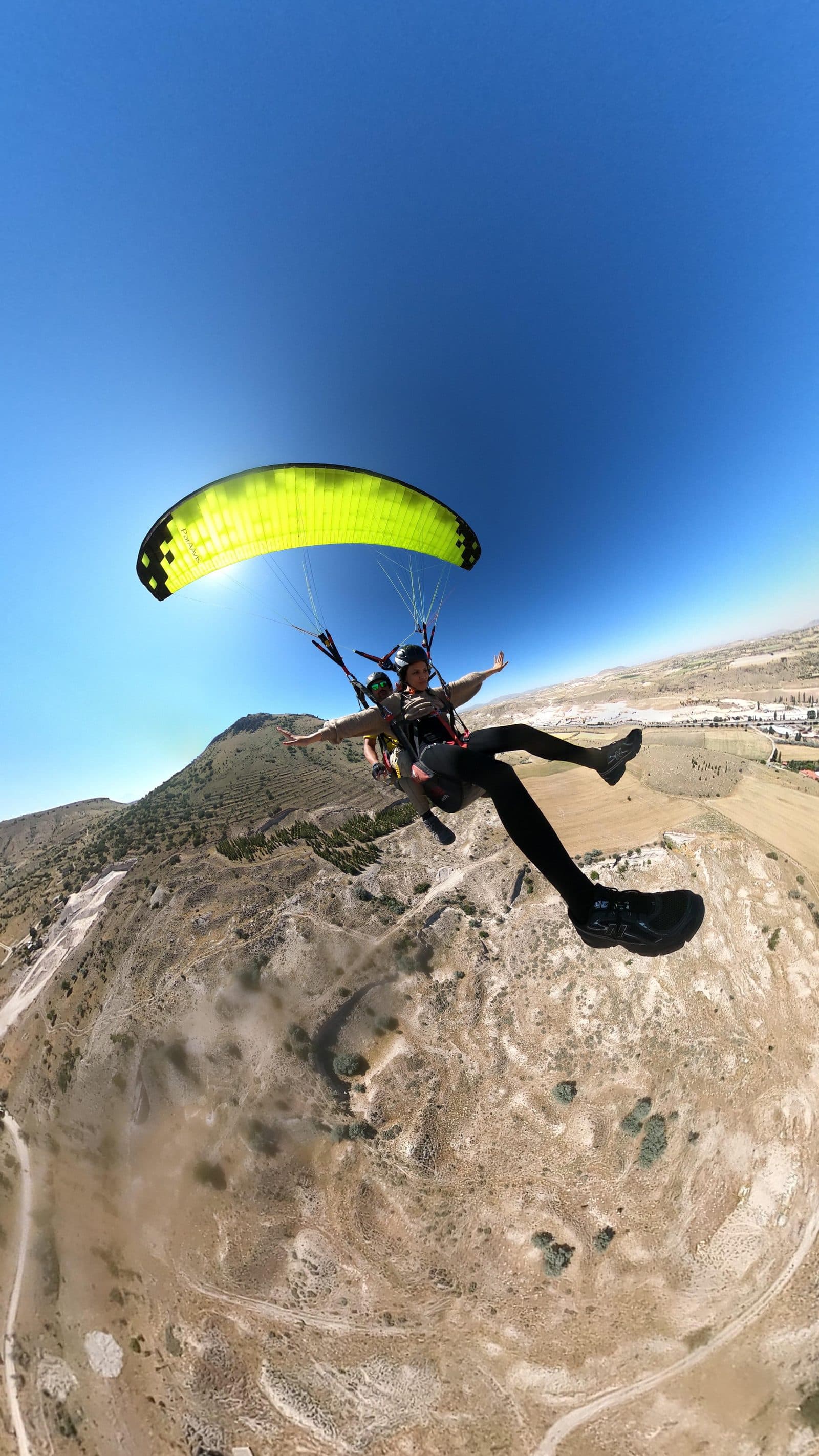 A tandem pair banking above a ridge. Tandem Paragliding, arranged from The Owl Cave Hotel in Göreme, Cappadocia.