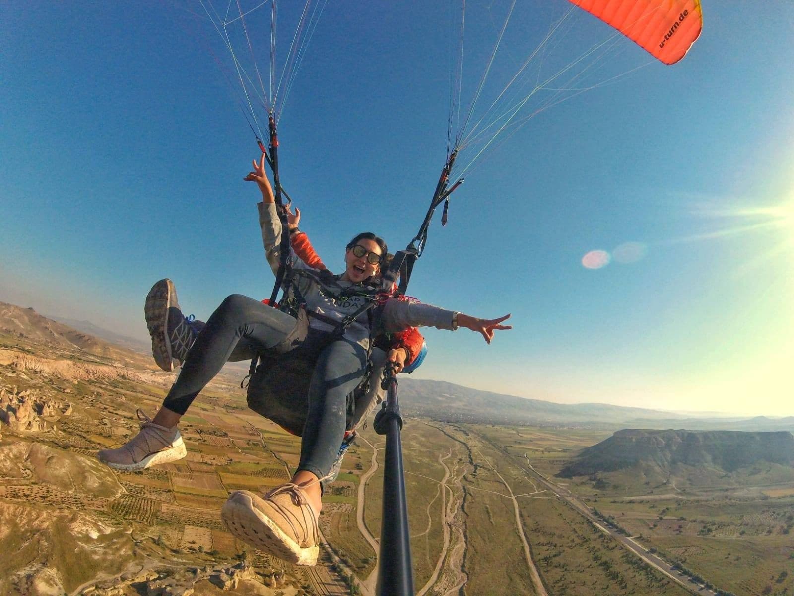 A tandem pair above fields and a road. Tandem Paragliding, arranged from The Owl Cave Hotel in Göreme, Cappadocia.