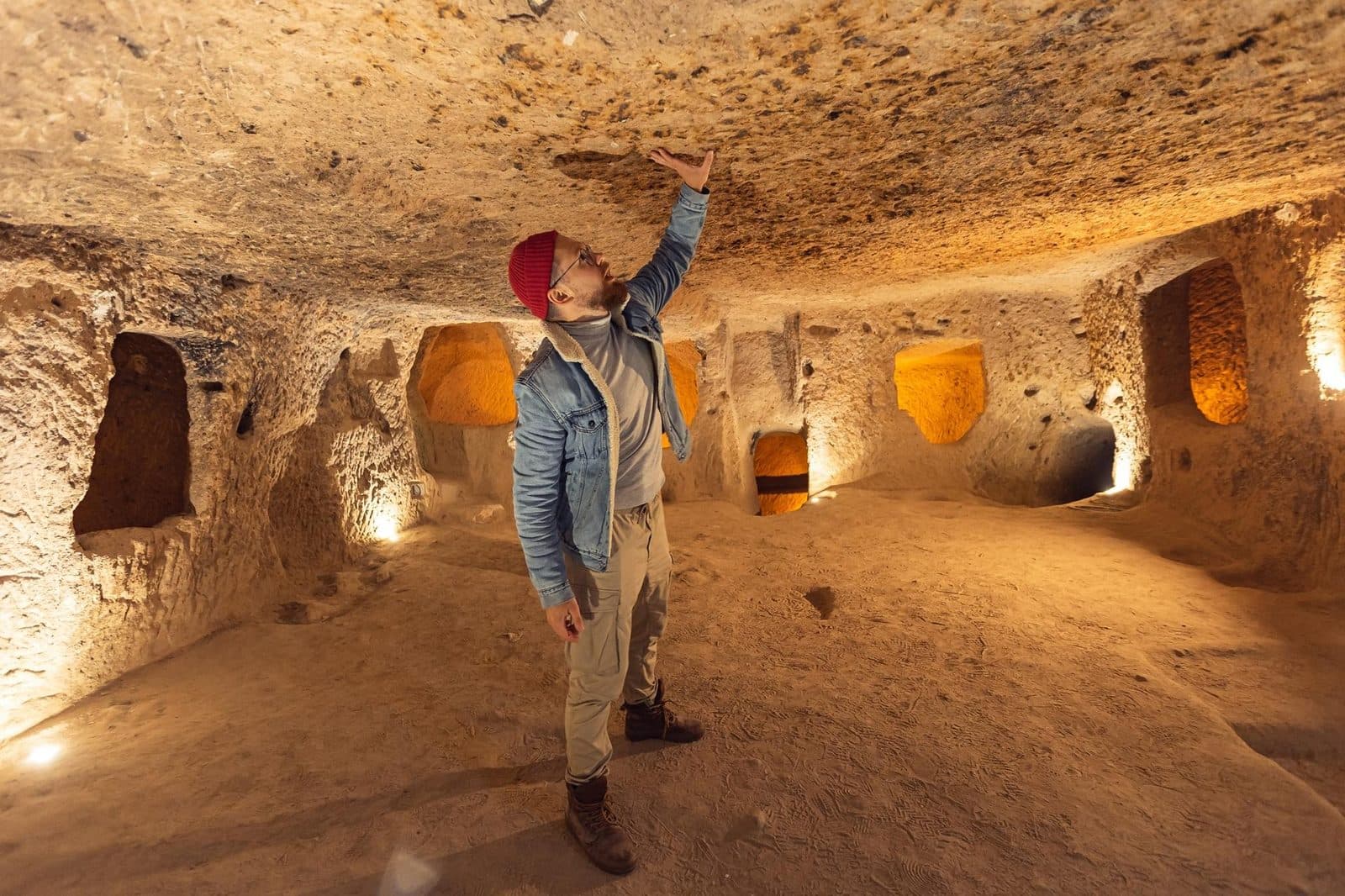 A visitor in a red cap pointing up at a cave ceiling. Cappadocia Red and Green Day, arranged from The Owl Cave Hotel in Göreme, Cappadocia.