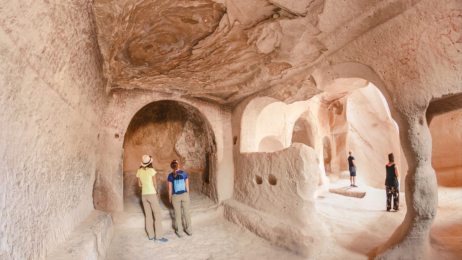 Two visitors inside a pale cave room cut with niches. Cappadocia Red and Green Day, arranged from The Owl Cave Hotel in Göreme, Cappadocia.