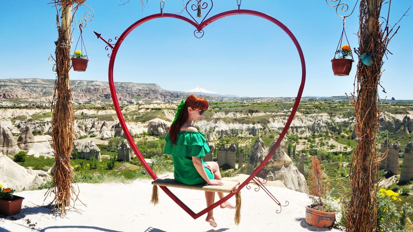 A guest under a red heart frame with fairy chimneys behind her. Cappadocia Red and Green Day, arranged from The Owl Cave Hotel in Göreme, Cappadocia.