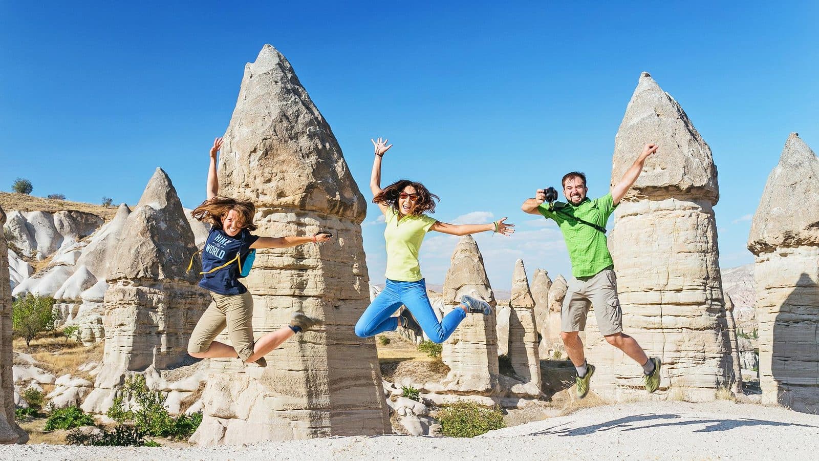 Three guests jumping in front of fairy chimneys. Cappadocia Red and Green Day, arranged from The Owl Cave Hotel in Göreme, Cappadocia.