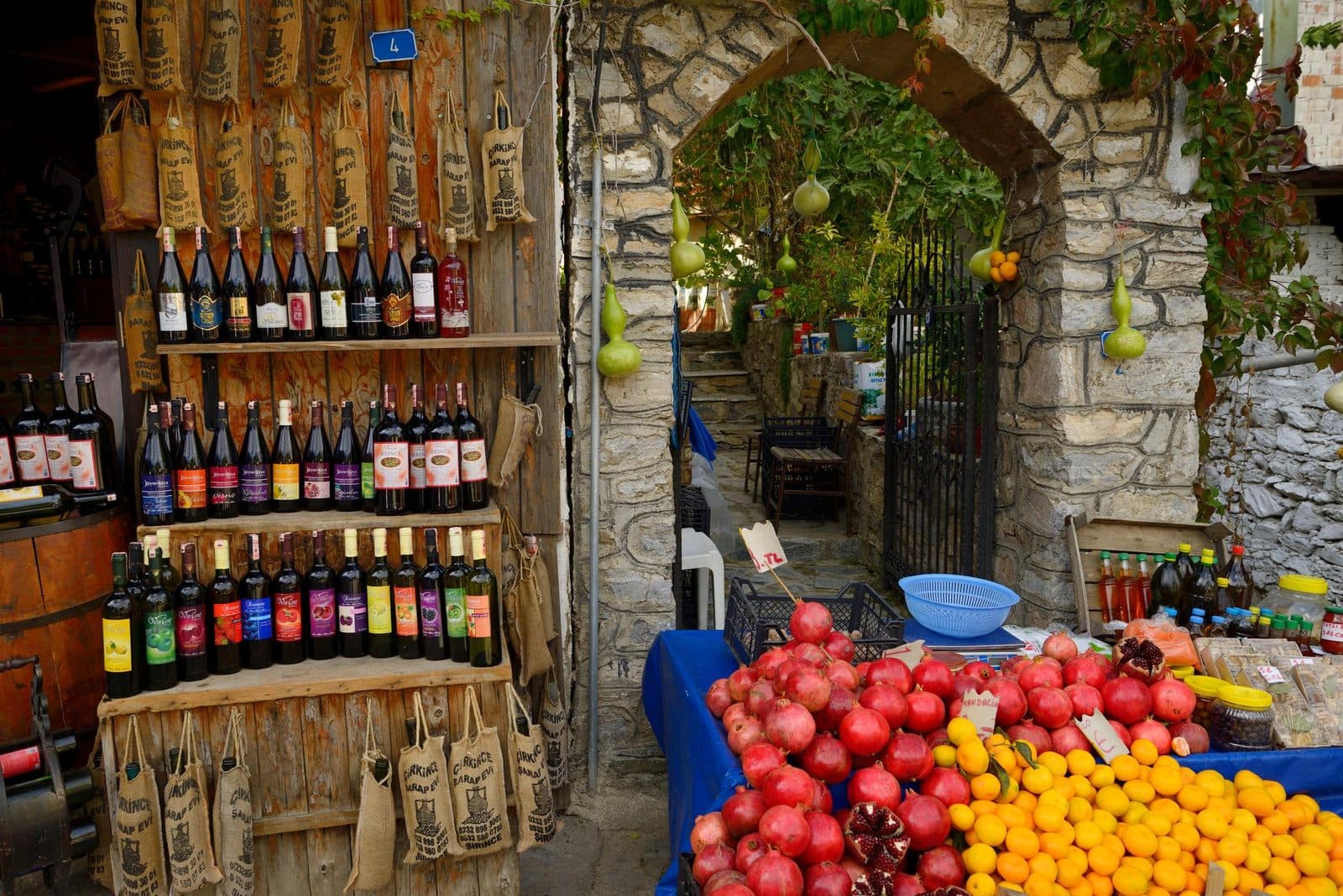 Shelves of wine bottles beside crates of fruit at a stone shop. Fairy Chimneys and Wine Tasting, arranged from The Owl Cave Hotel in Göreme, Cappadocia.