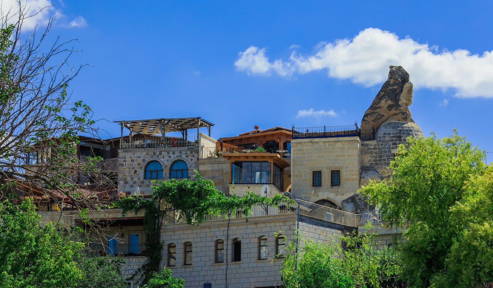 Stone cave houses with blue window frames and a fairy chimney. Sunrise or Sunset Jeep Safari, arranged from The Owl Cave Hotel in Göreme, Cappadocia.