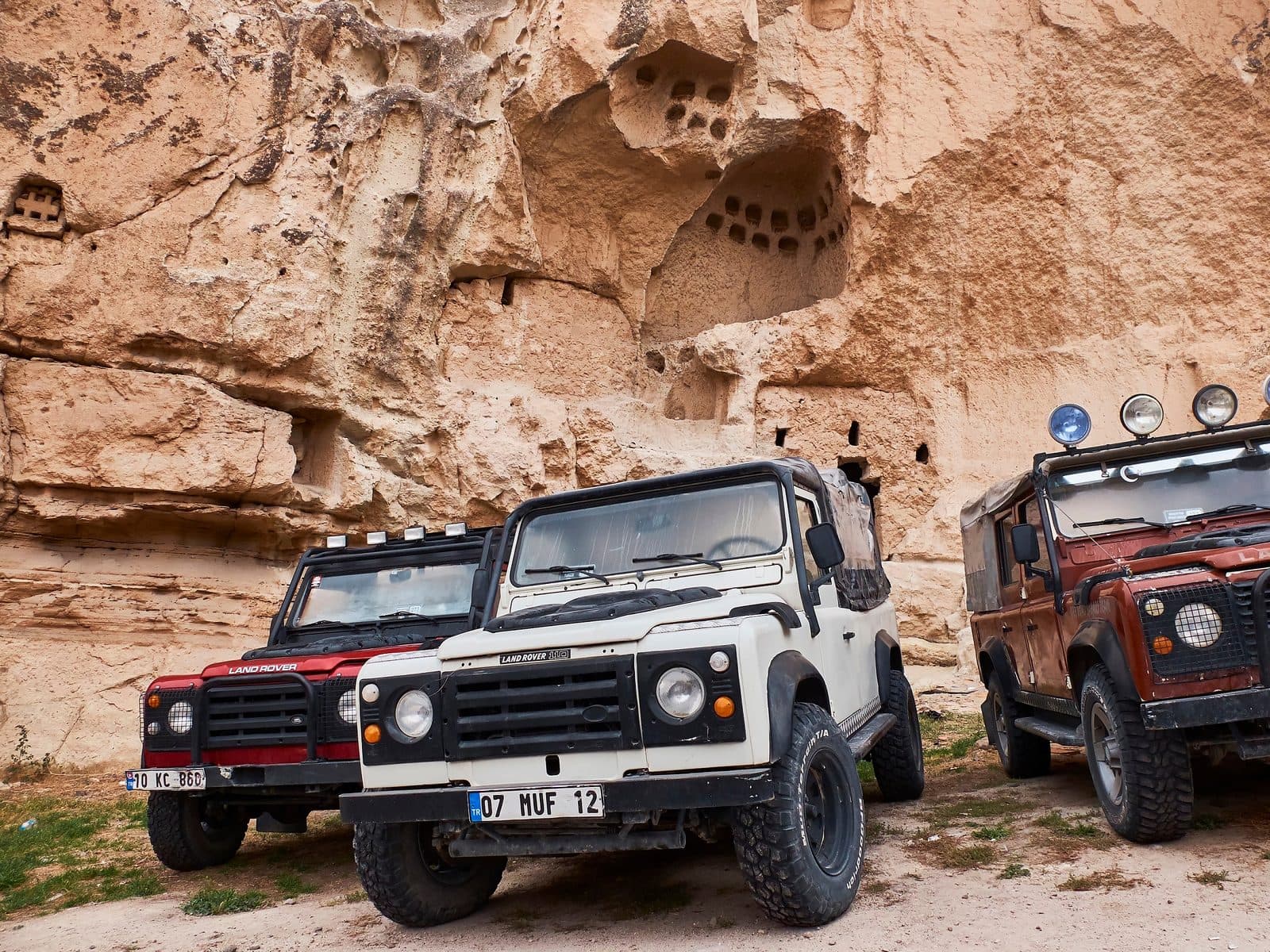 White, red, and black jeeps parked against a cave cliff. Sunrise or Sunset Jeep Safari, arranged from The Owl Cave Hotel in Göreme, Cappadocia.