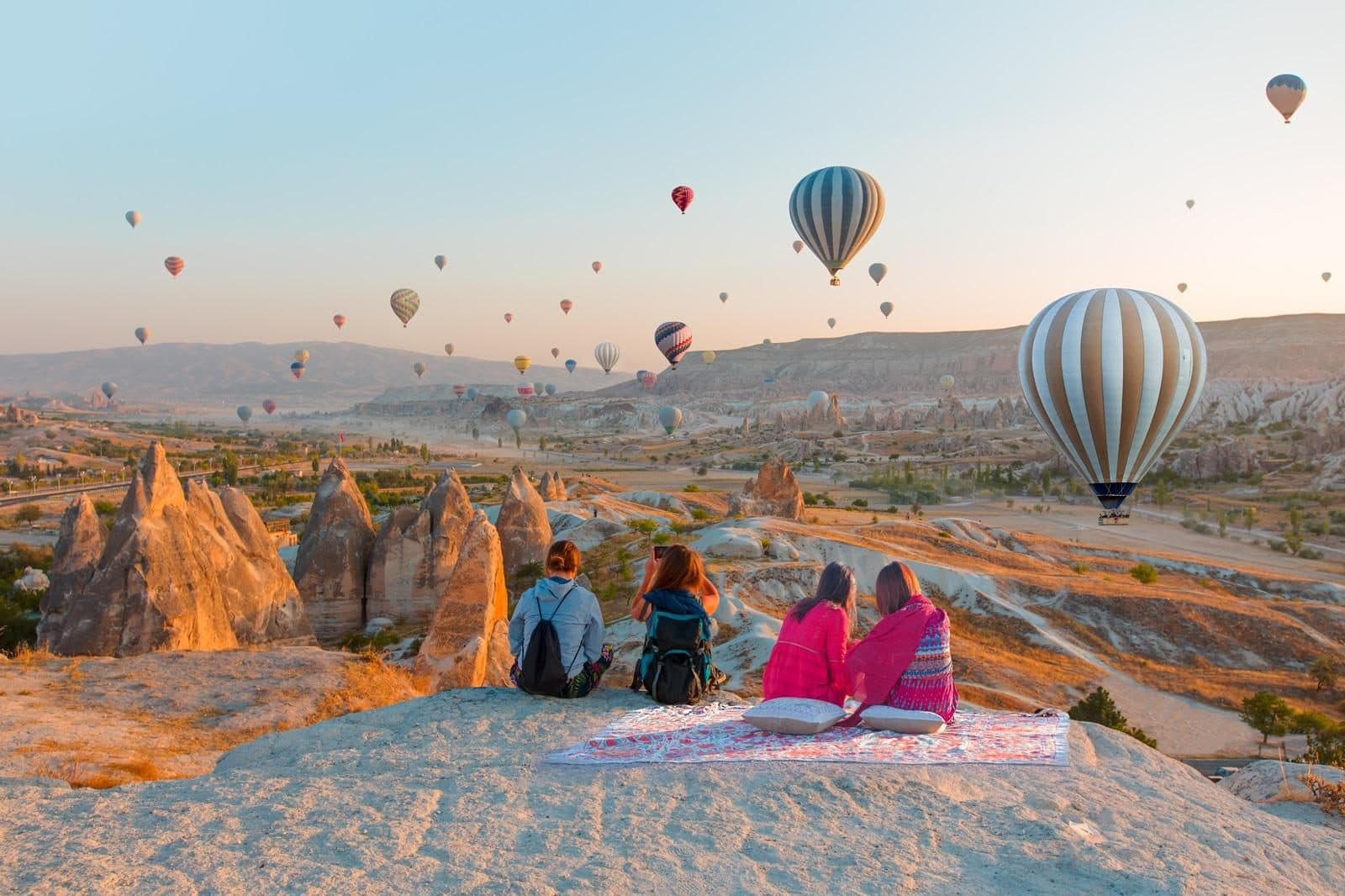 Two guests seated on a rock watching balloons. Sunrise Balloon Watching, arranged from The Owl Cave Hotel in Göreme, Cappadocia.