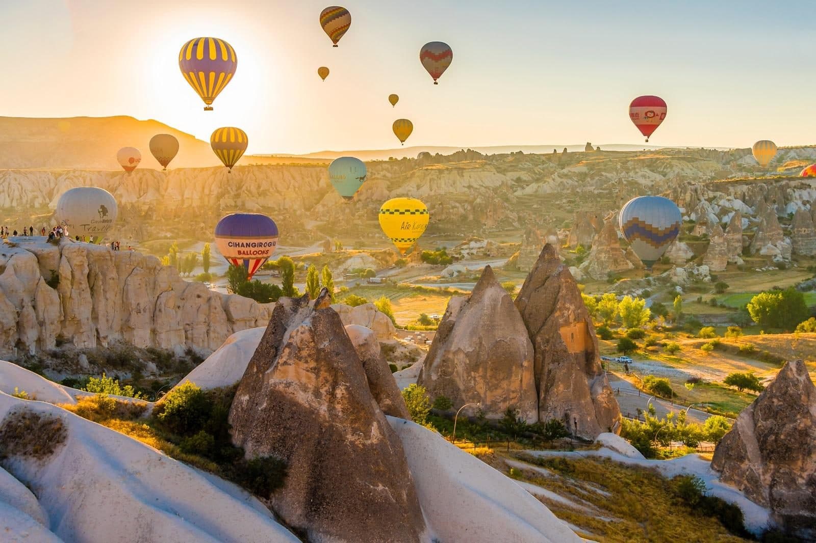 Hot air balloons at sunrise over fairy chimneys and a village. Sunrise Balloon Watching, arranged from The Owl Cave Hotel in Göreme, Cappadocia.