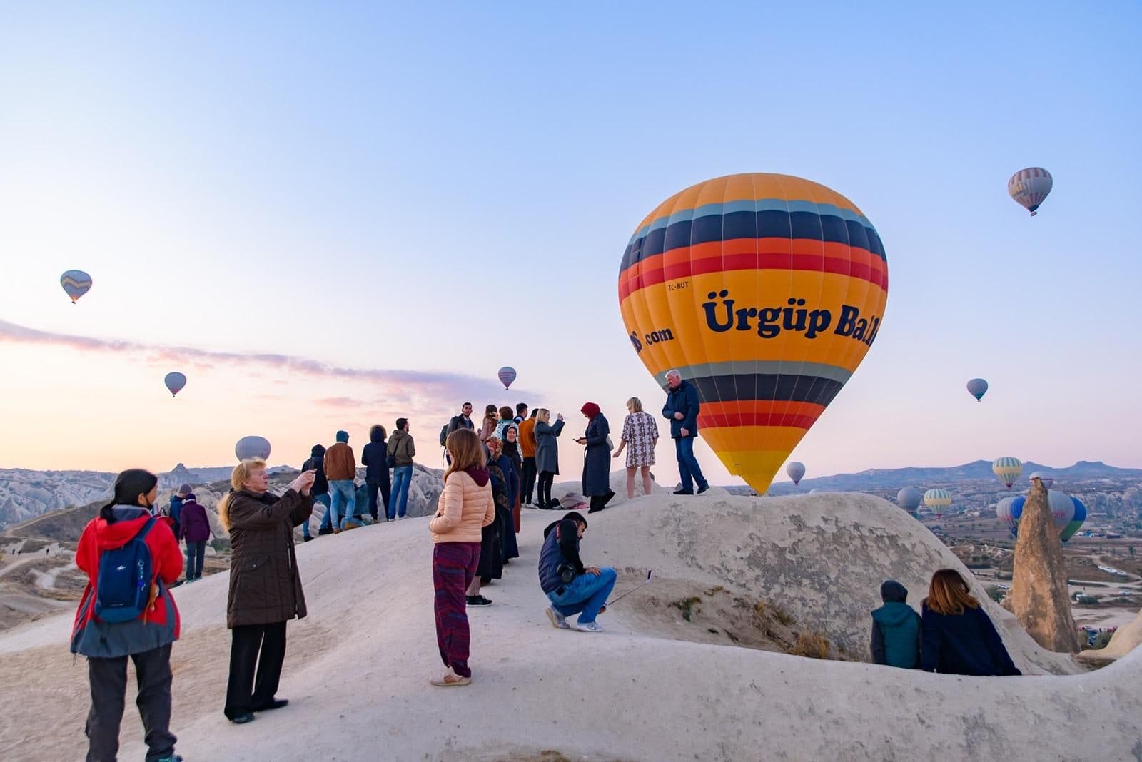 A group beside a yellow balloon marked Ürgüp. Sunrise Balloon Watching, arranged from The Owl Cave Hotel in Göreme, Cappadocia.
