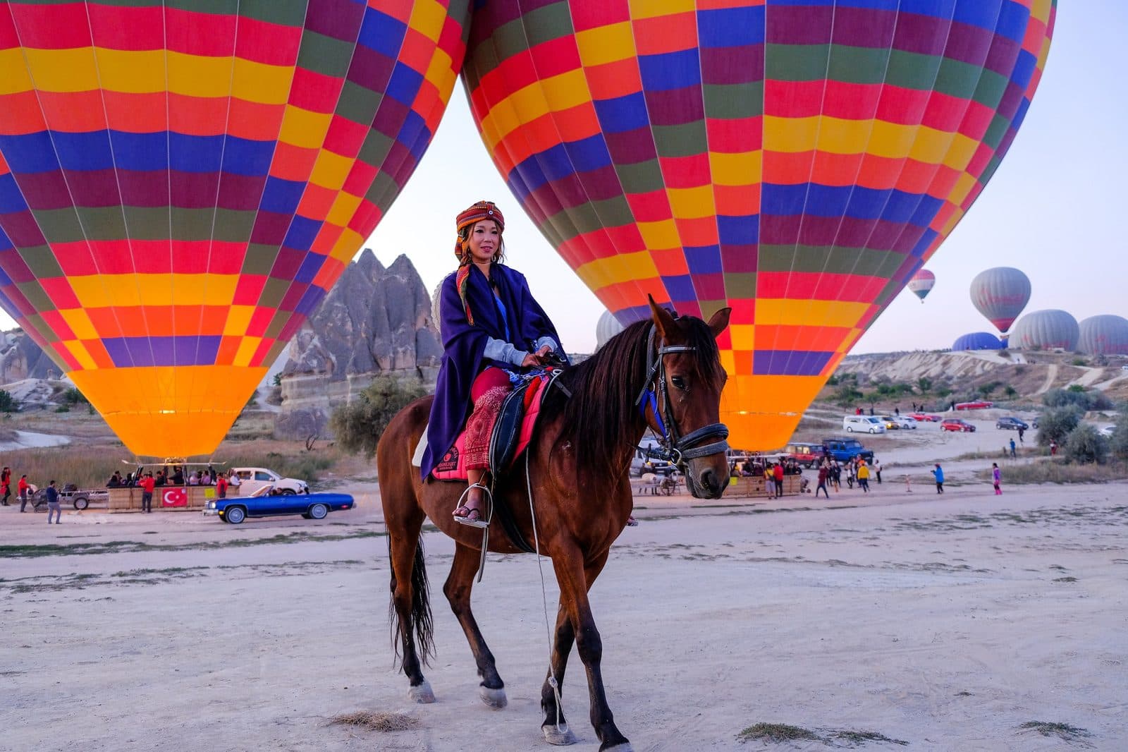 A rider in red beside two large colorful balloons. Sunrise Horse Ride, arranged from The Owl Cave Hotel in Göreme, Cappadocia.