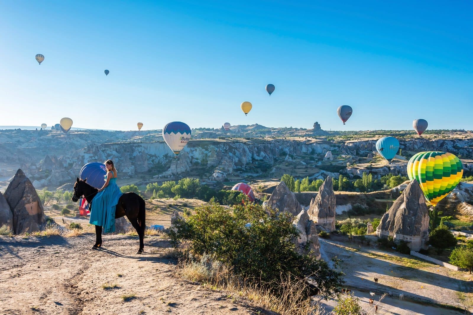 A rider in blue beside a balloon envelope on a track. Sunrise Horse Ride, arranged from The Owl Cave Hotel in Göreme, Cappadocia.