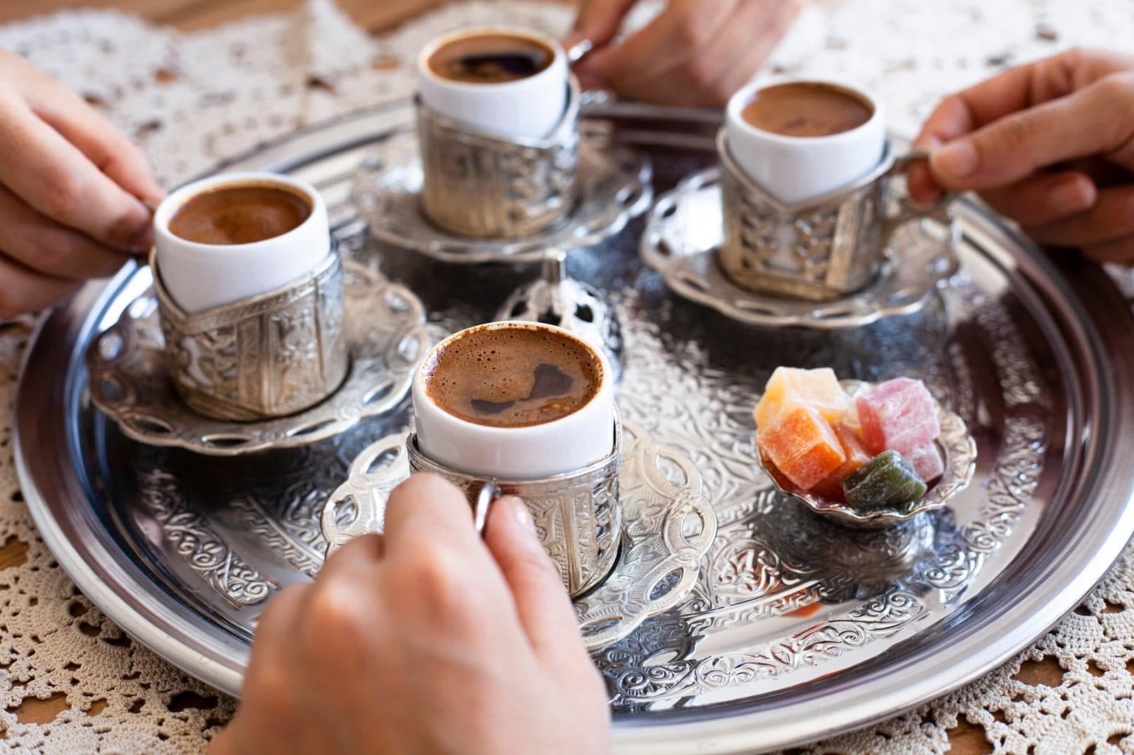 Hands taking cups of Turkish coffee from a silver tray with lokum. Sand-Brewed Turkish Coffee Workshop, arranged from The Owl Cave Hotel in Göreme, Cappadocia.