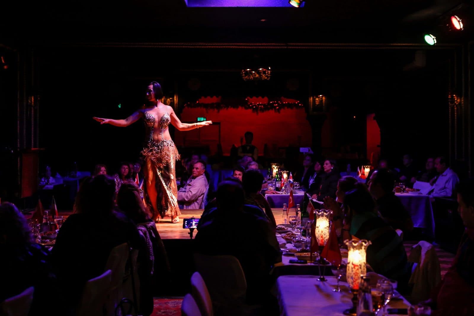 A belly dancer on a small stage, with diners at candlelit tables. Turkish Night at a Cave Restaurant, arranged from The Owl Cave Hotel in Göreme, Cappadocia.