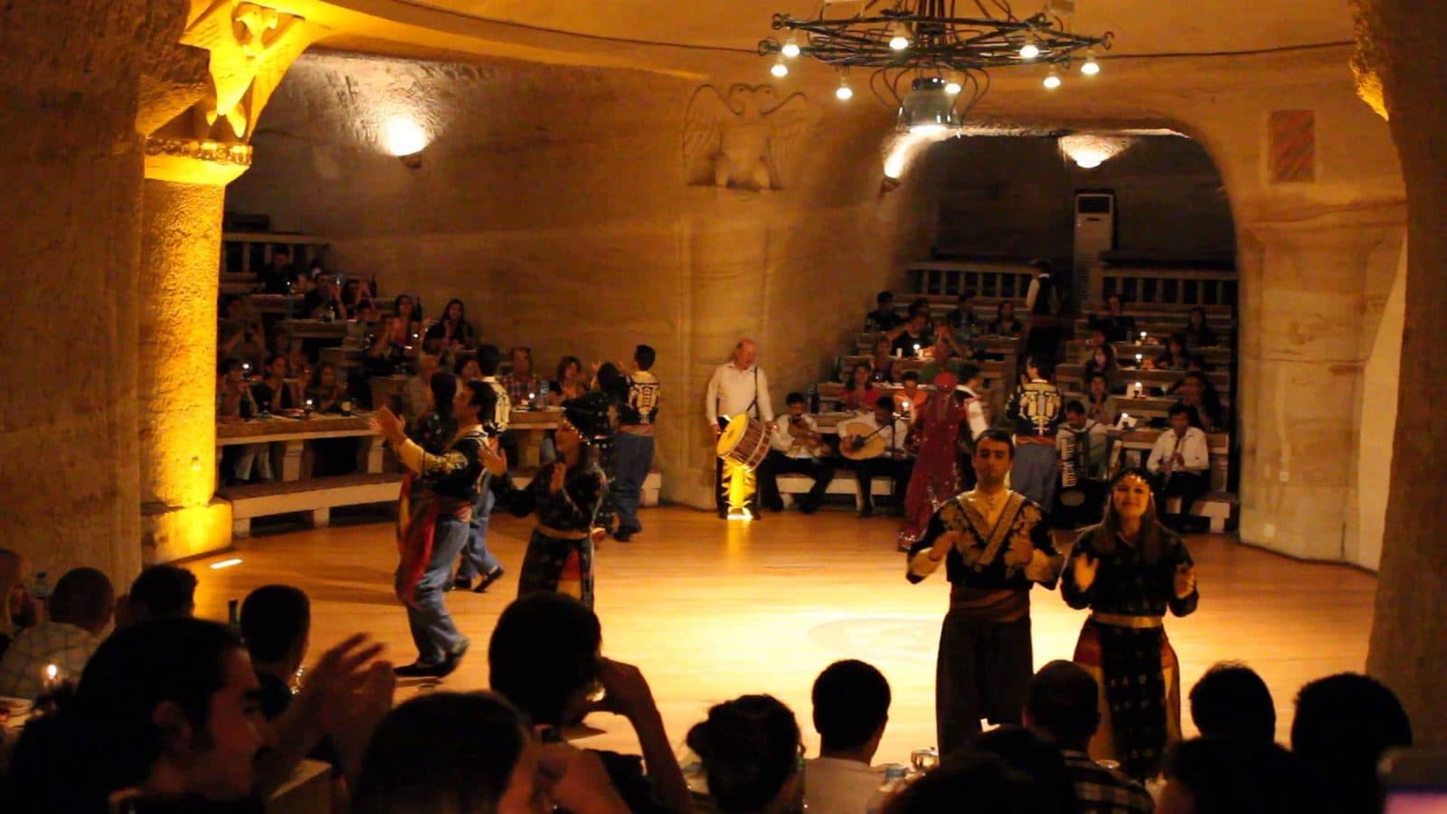 Diners watching dancers in a cave room with stone columns. Turkish Night at a Cave Restaurant, arranged from The Owl Cave Hotel in Göreme, Cappadocia.