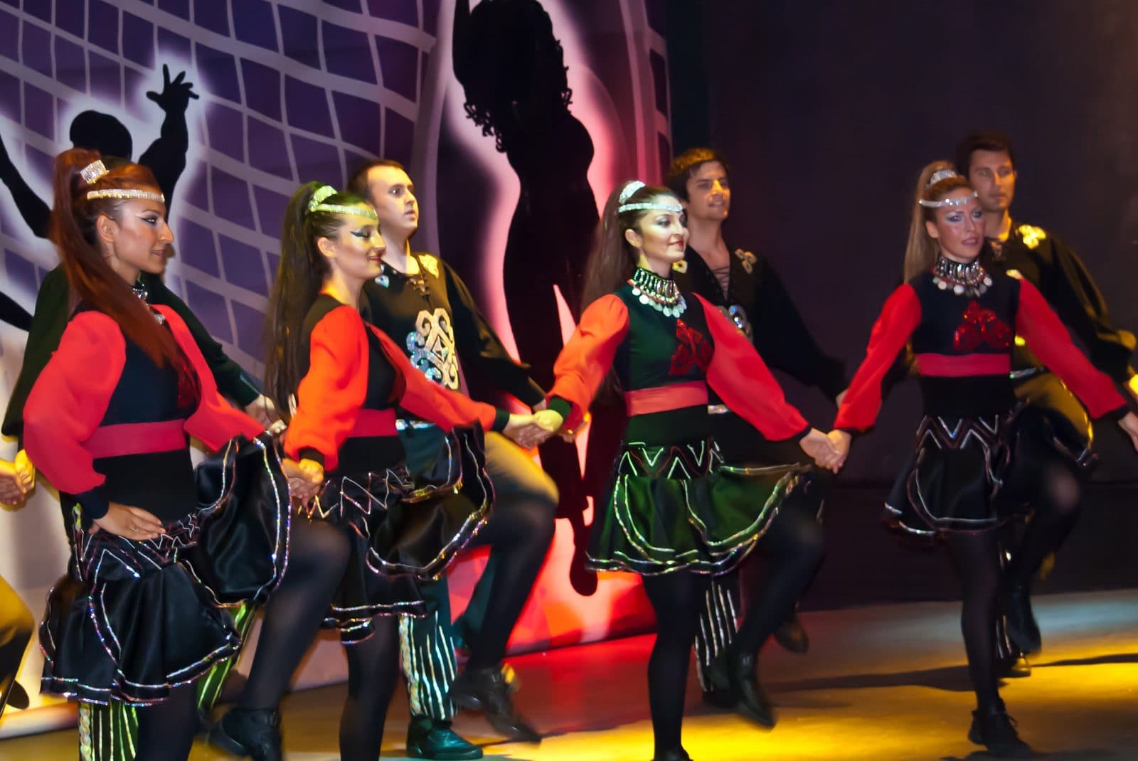 Folk dancers in red and green holding hands on stage. Turkish Night at a Cave Restaurant, arranged from The Owl Cave Hotel in Göreme, Cappadocia.