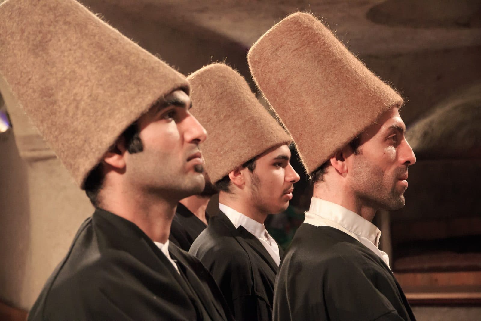 Three whirling dervishes in profile, wearing tall hats. Whirling Dervish Ceremony and Dinner, arranged from The Owl Cave Hotel in Göreme, Cappadocia.