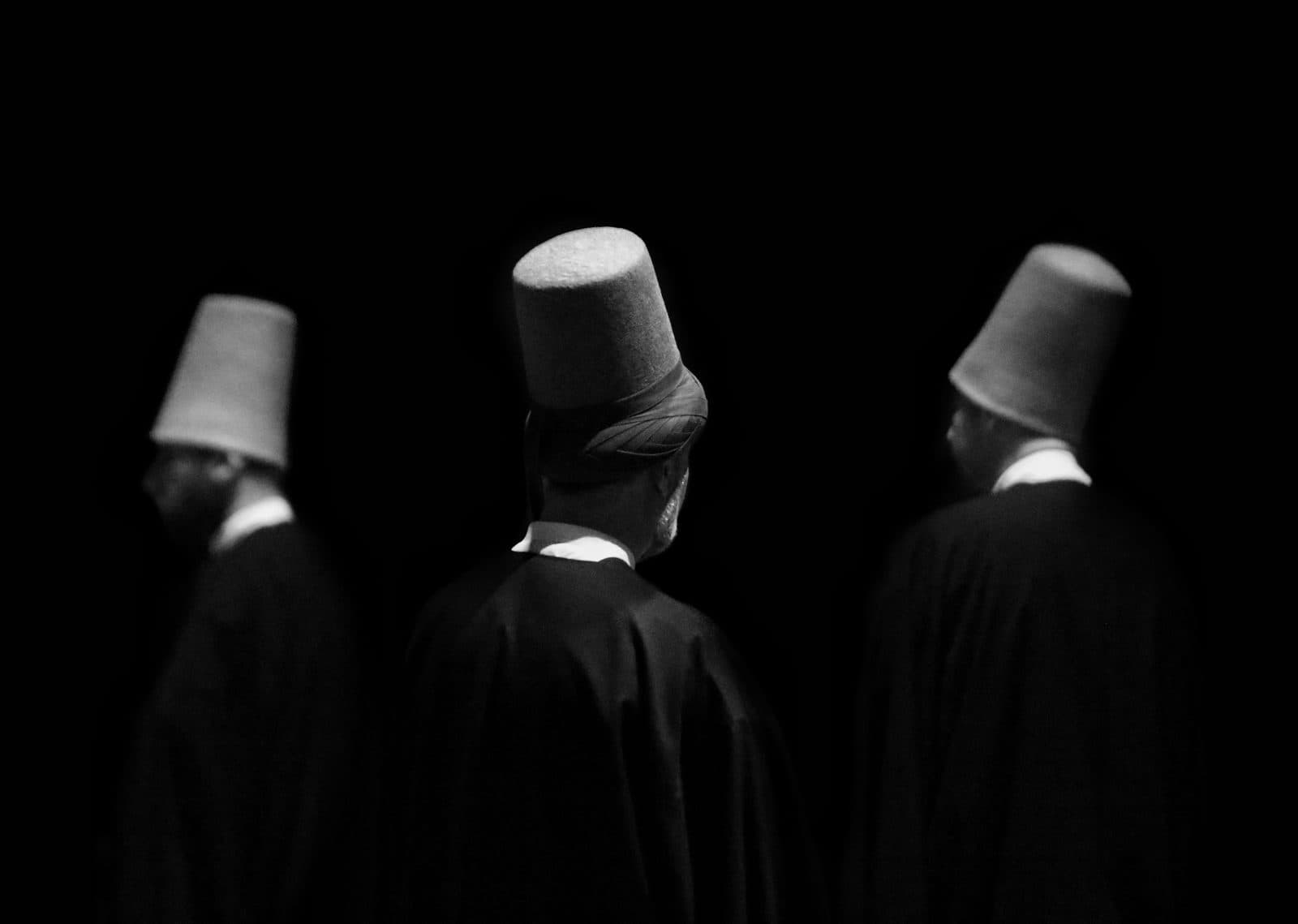 Whirling dervishes seen from behind in tall white hats. Whirling Dervish Ceremony and Dinner, arranged from The Owl Cave Hotel in Göreme, Cappadocia.