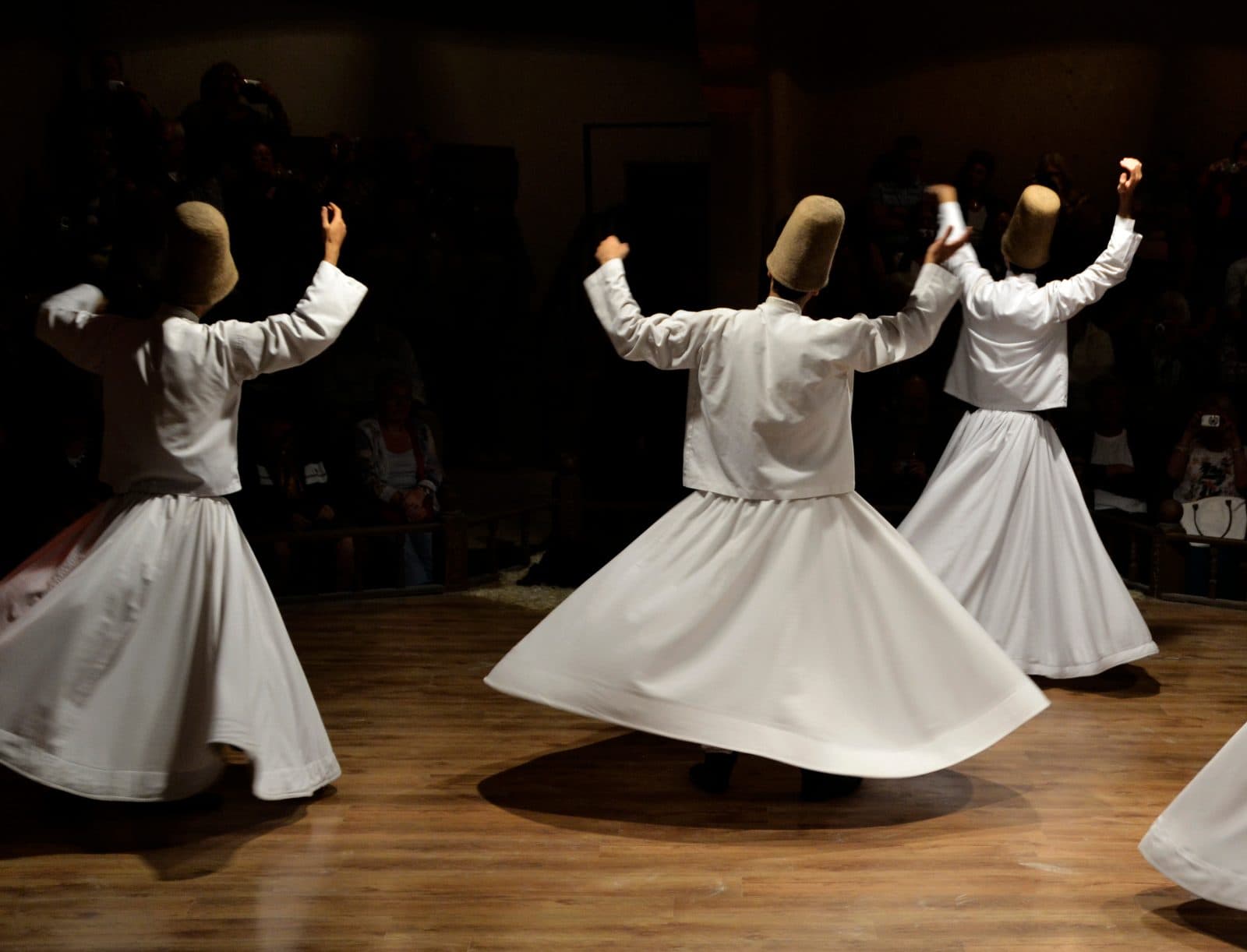 Whirling dervishes in white robes spinning on a wooden stage. Whirling Dervish Ceremony and Dinner, arranged from The Owl Cave Hotel in Göreme, Cappadocia.